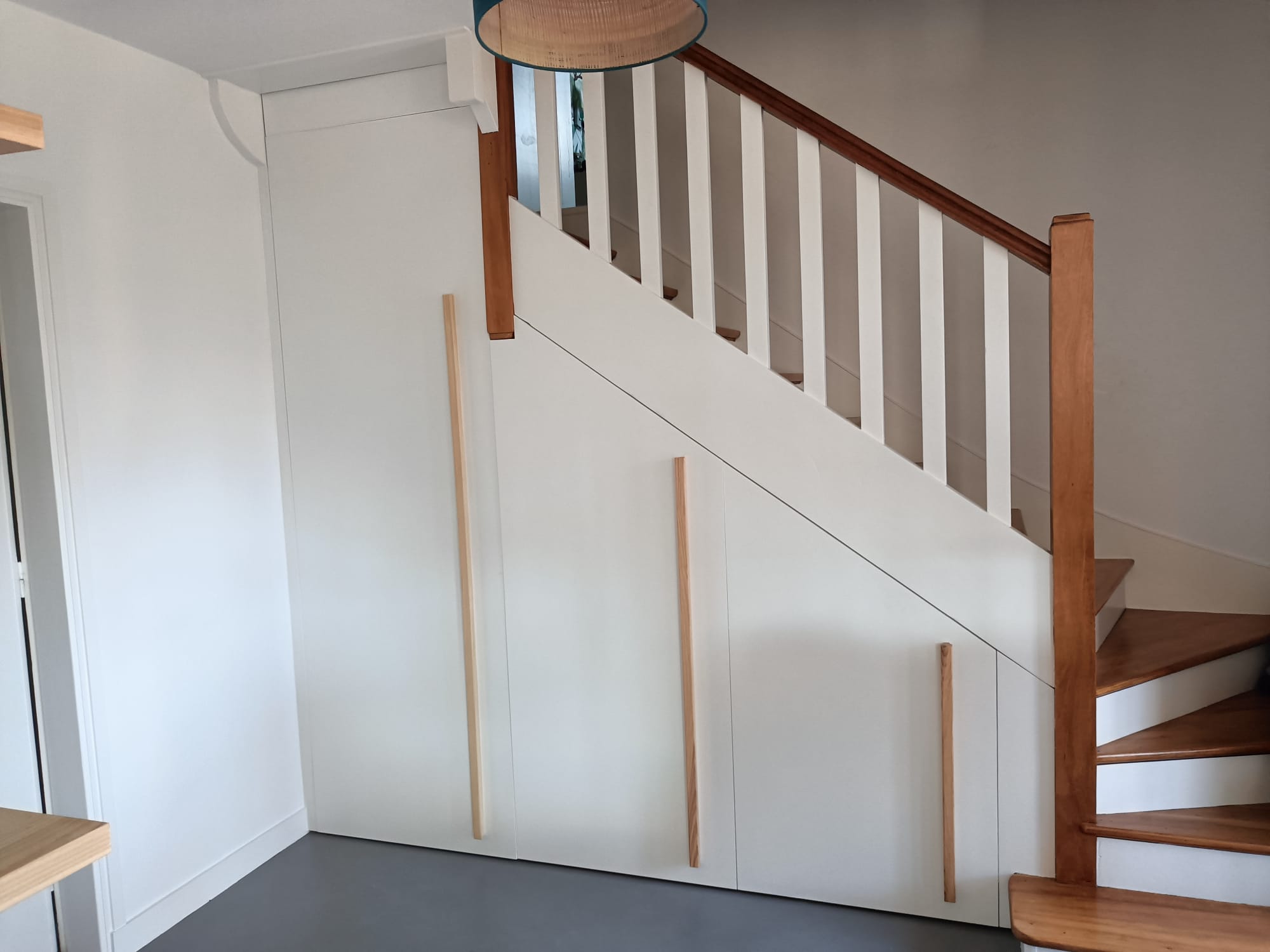 A Saint-Coulomb, agencement d'un placard / dressing sous escalier, avec porte battante et ensemble coulissant.  Fabriqué en MDF peint en blanc et fabrication de poignées en frêne massif. par Hugo Pauchard - HP Bois Menuiserie - Saint-Malo